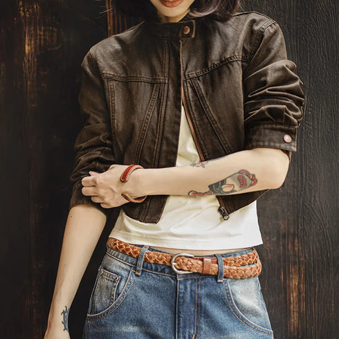Person wearing a brown jacket, white shirt, blue jeans, and a braided belt against a dark wooden background.